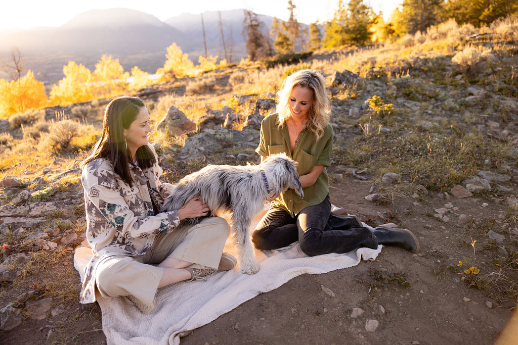 Dr. Holly Hickman and Dr. Julie McKenzie with Jerry at golden hour on a Summit County hillside, with mountains in the distance